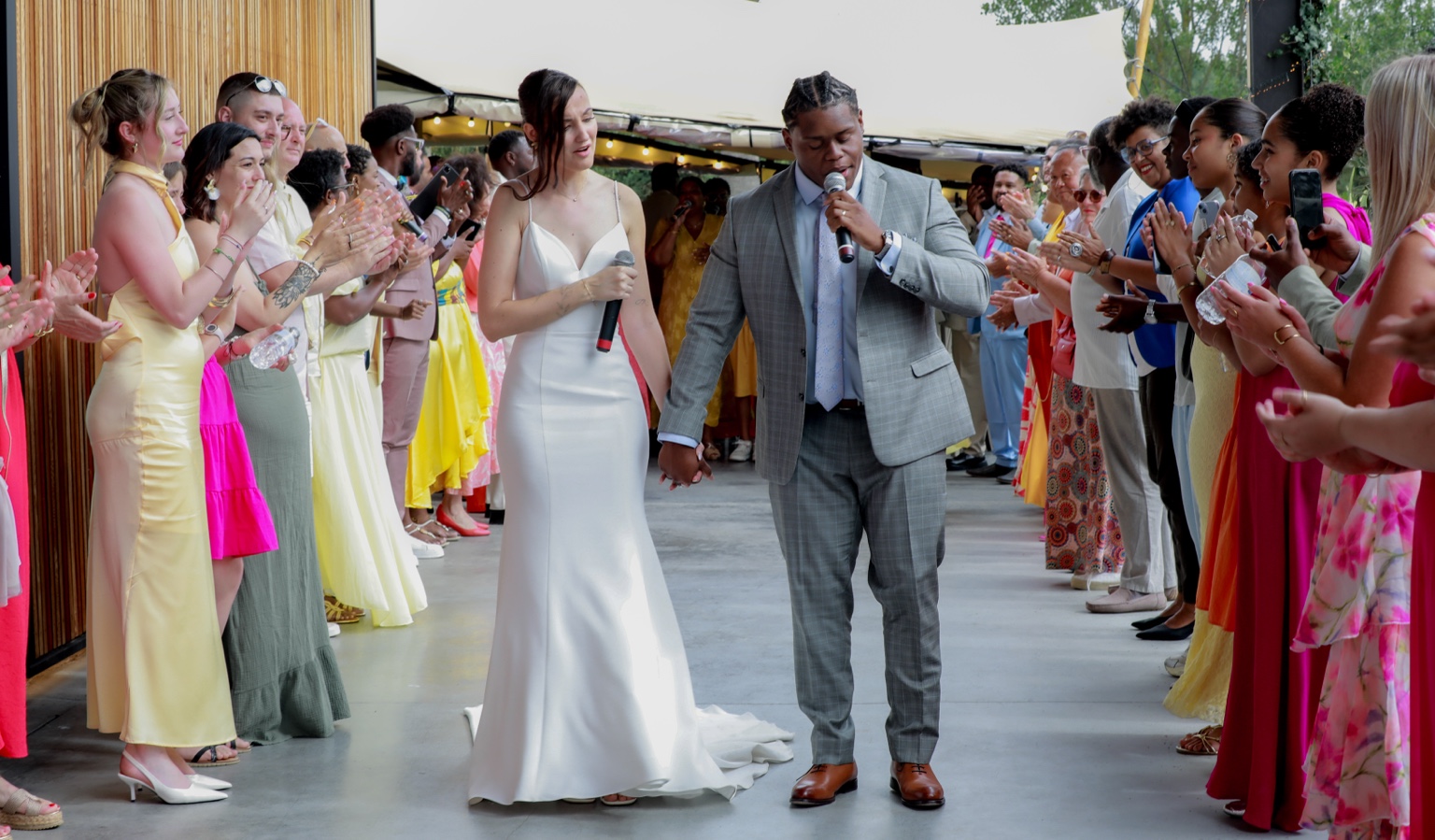 Marina et Anthony main dans la main avec leurs micros, entourés des invités qui applaudissent